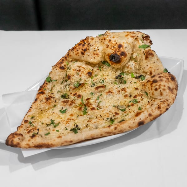 Garlic naan breads garnished with cilantro and herbs, stacked on a white plate.
