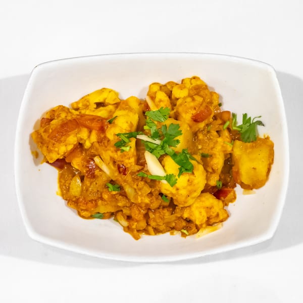 Golden cauliflower curry with tomatoes and onions, garnished with fresh cilantro, served in a white dish.