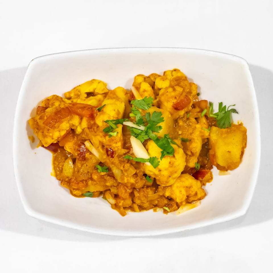 Golden cauliflower curry with tomatoes and onions, garnished with fresh cilantro, served in a white dish.