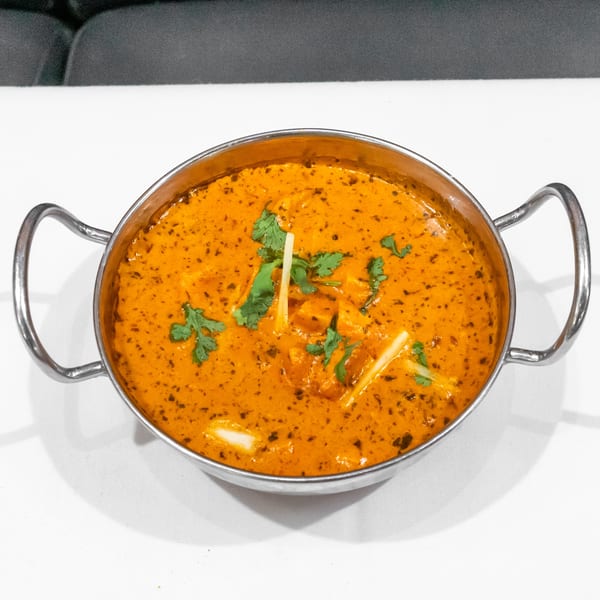 Creamy orange curry garnished with cilantro and ginger strips, served in a handled metal bowl on a white tablecloth.