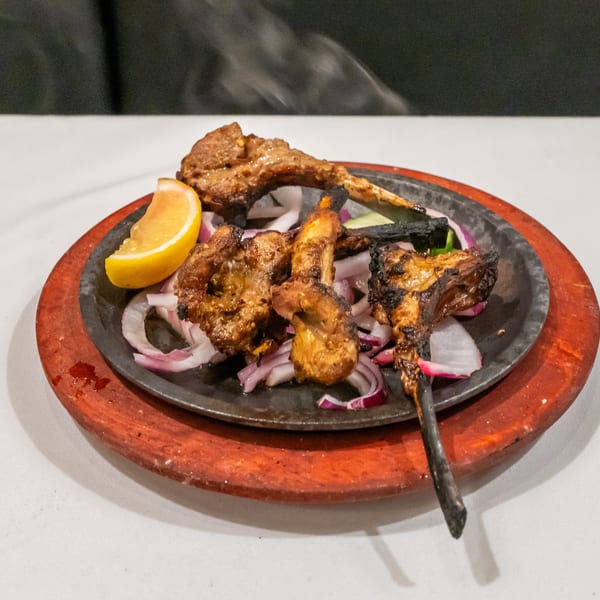 Chargrilled meat and vegetables served with red onions and lemon on a black platter.