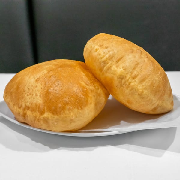 Three golden-brown bread rolls arranged on a white plate against a dark background.