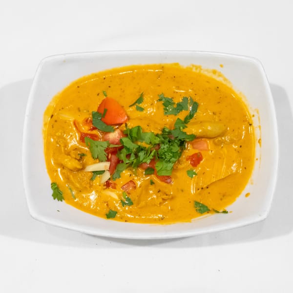 Creamy orange curry topped with chopped cilantro, diced tomatoes, and sliced vegetables in a white rectangular dish.