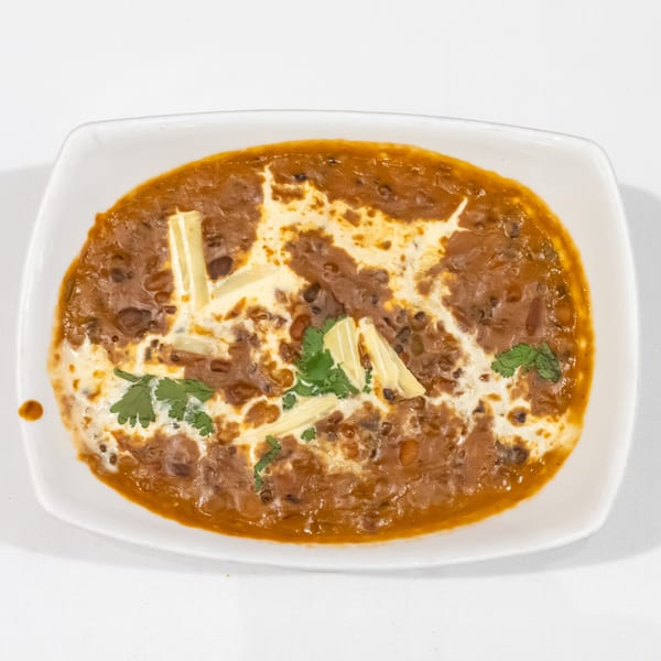 Creamy spiced lentil curry garnished with butter and cilantro, served in a white rectangular dish.