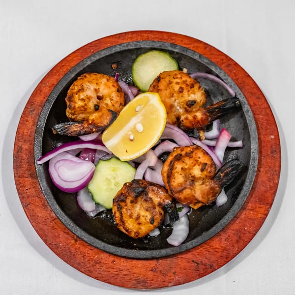 Grilled spiced shrimp arranged on a sizzling platter with lemon, cucumber, and sliced red onions.