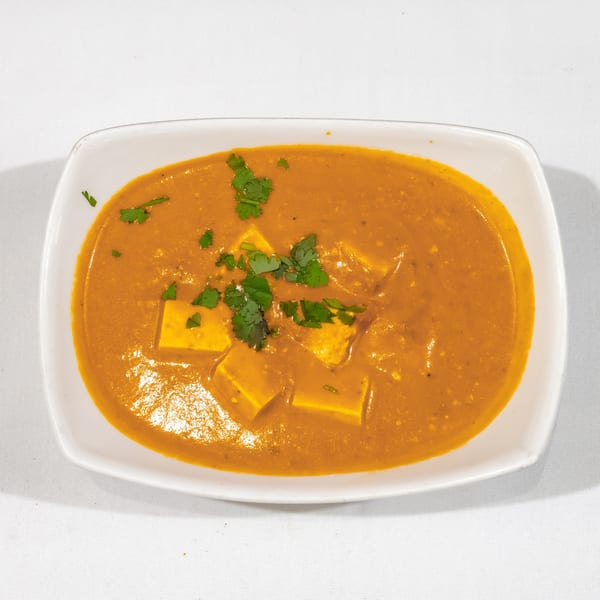 Creamy Indian paneer curry garnished with fresh cilantro, served in a white rectangular dish.
