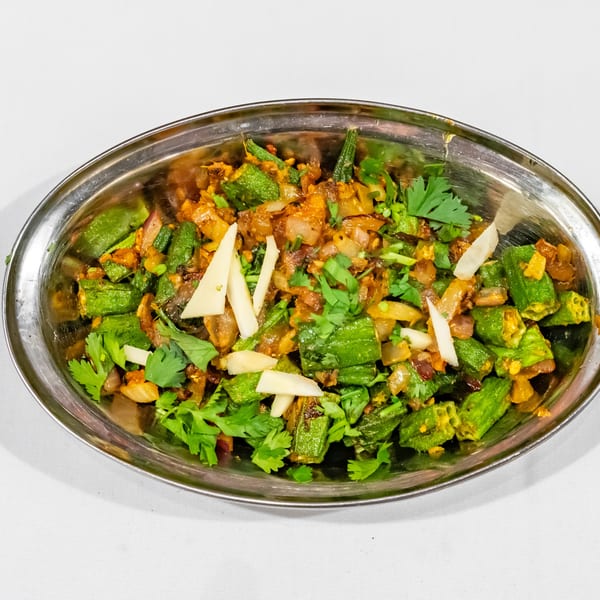 Spiced okra and vegetable dish garnished with fresh cilantro and ginger in a polished oval metal serving dish.