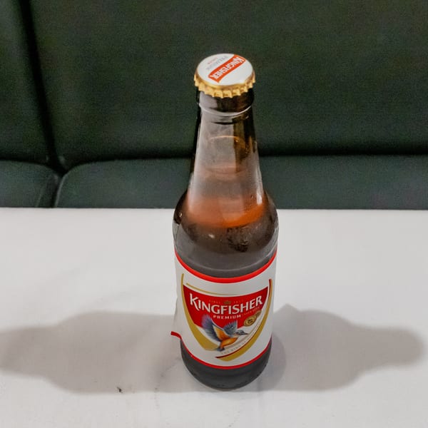 Kingfisher Premium Lager beer bottle on a white table against a dark upholstered background.