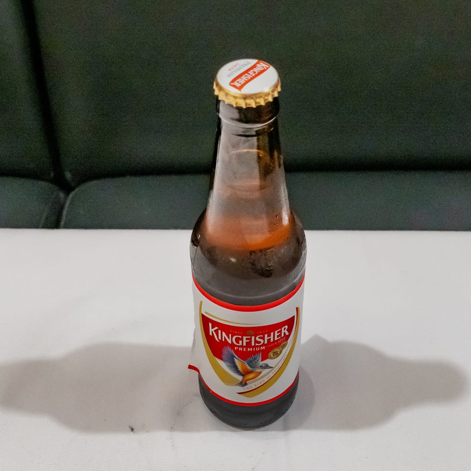 Kingfisher Premium Lager beer bottle on a white table against a dark upholstered background.