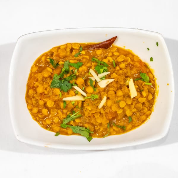 Golden chickpea curry garnished with cilantro, sliced ginger, and a dried red chili on a white plate.