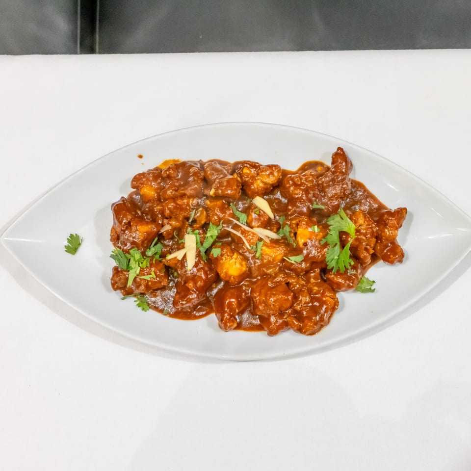 Spicy saucy chicken pieces garnished with cilantro and ginger on a white oval plate.