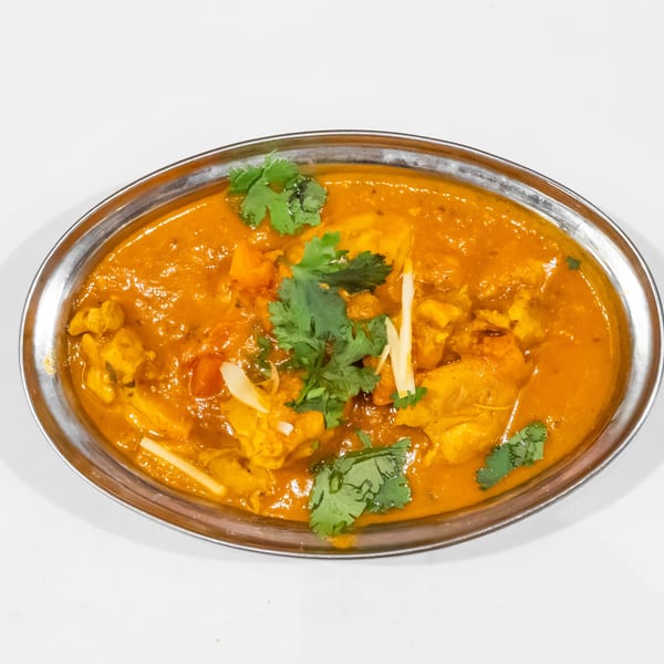 Creamy orange Indian curry with chunks of meat, garnished with fresh cilantro and julienned ginger in a metal serving dish.