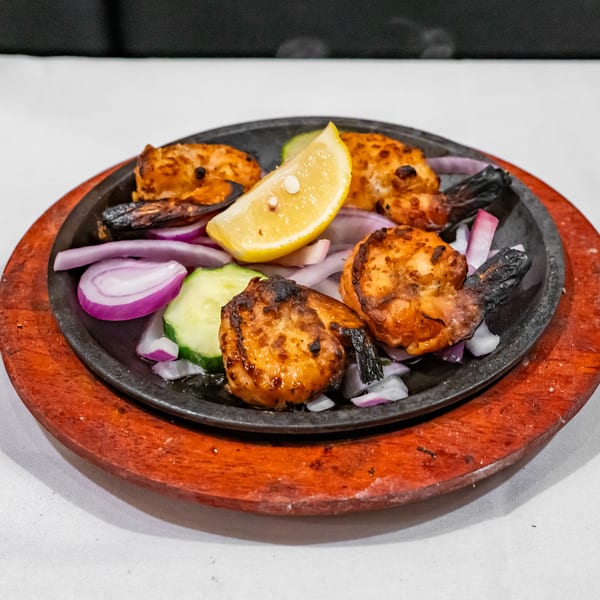 Grilled shrimp and vegetables with lemon, red onion, and cucumber served on a sizzling black platter.