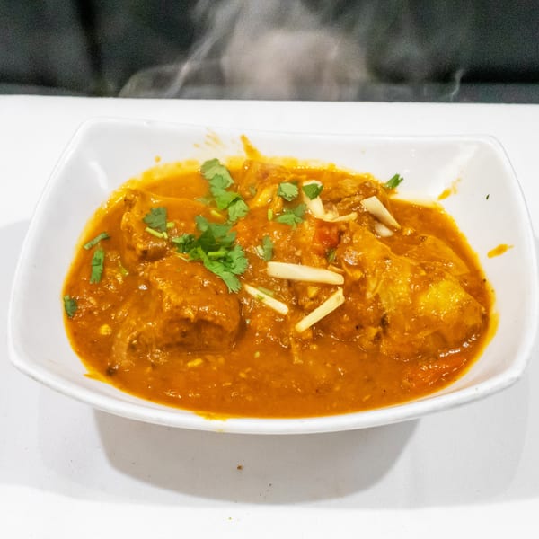 Rich orange curry with tender meat pieces, cilantro, and sliced ginger served in a white rectangular bowl.