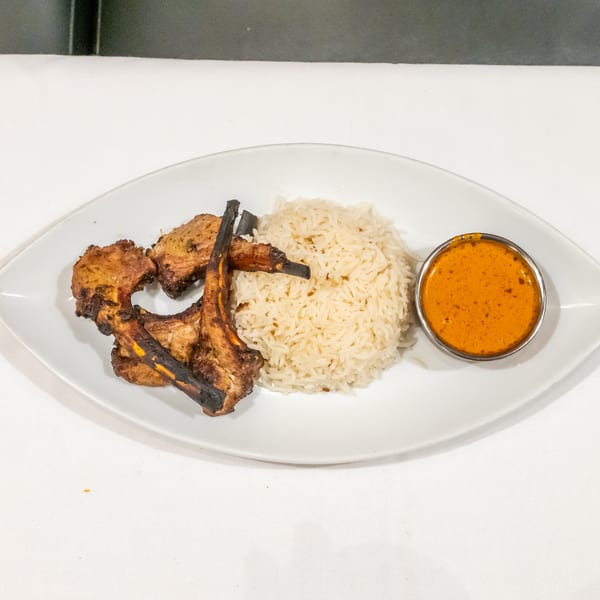 Grilled meat skewers served with basmati rice and orange dipping sauce on a white oval plate.
