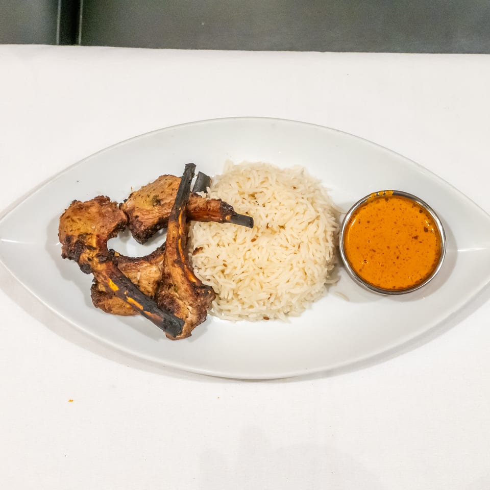 Grilled meat skewers served with basmati rice and orange dipping sauce on a white oval plate.