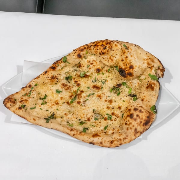 Garlic naan topped with herbs and sesame seeds, served on a white plate.