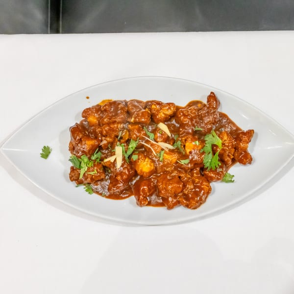 Saucy Indian-style chicken pieces garnished with fresh cilantro and ginger strips on a white oval plate.