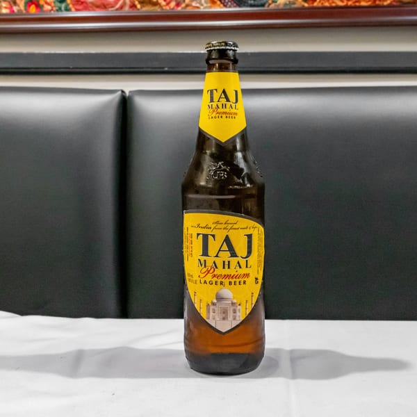 Taj Mahal Premium Lager beer bottle displayed on a white table against a dark upholstered restaurant booth.