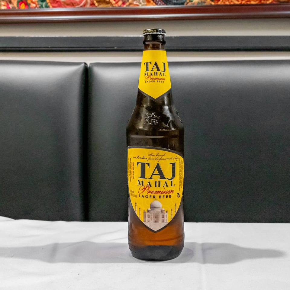 Taj Mahal Premium Lager beer bottle displayed on a white table against a dark upholstered restaurant booth.