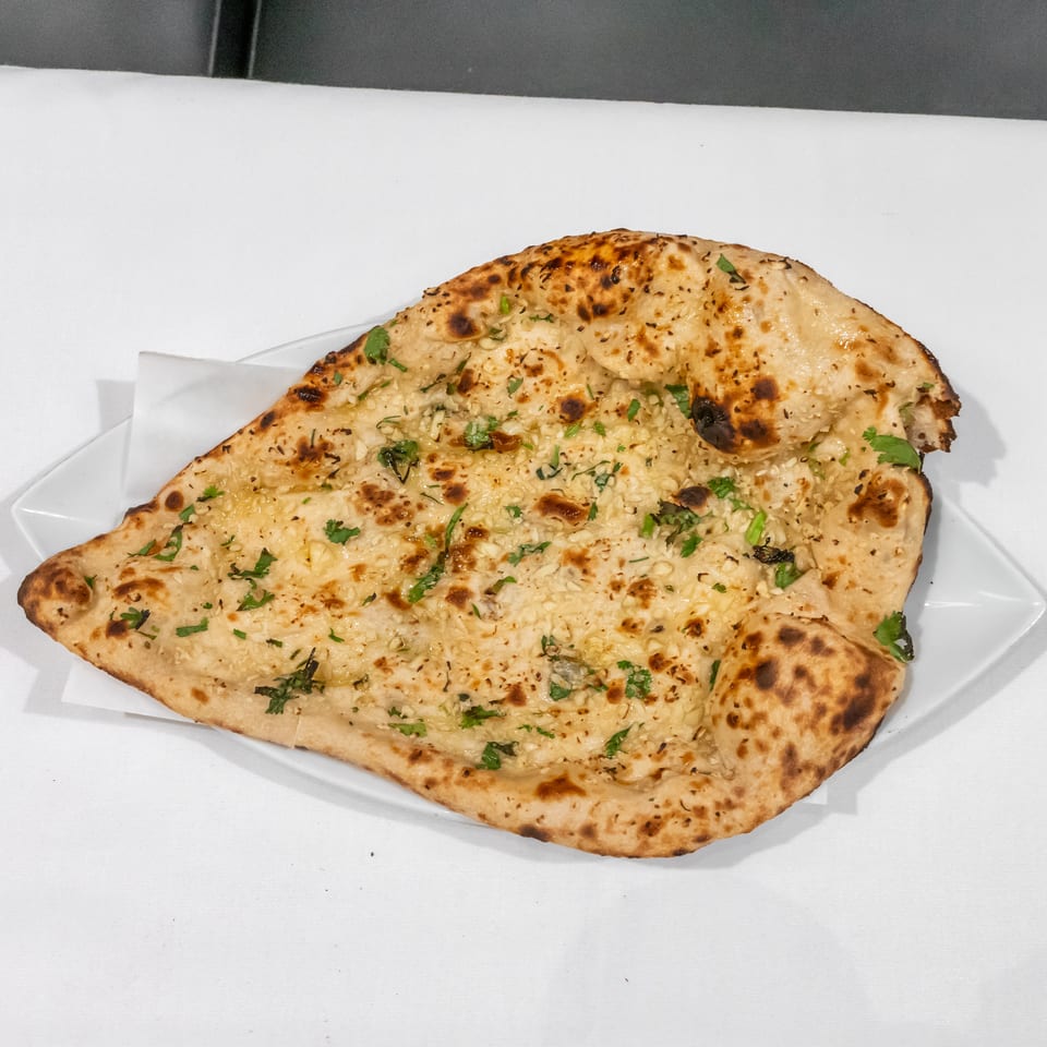 Garlic naan bread garnished with cilantro, served on a white plate.