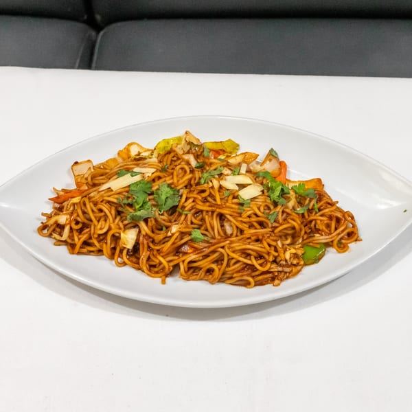 Stir-fried noodles with cabbage, carrots, onions, and cilantro served on a white oval plate.