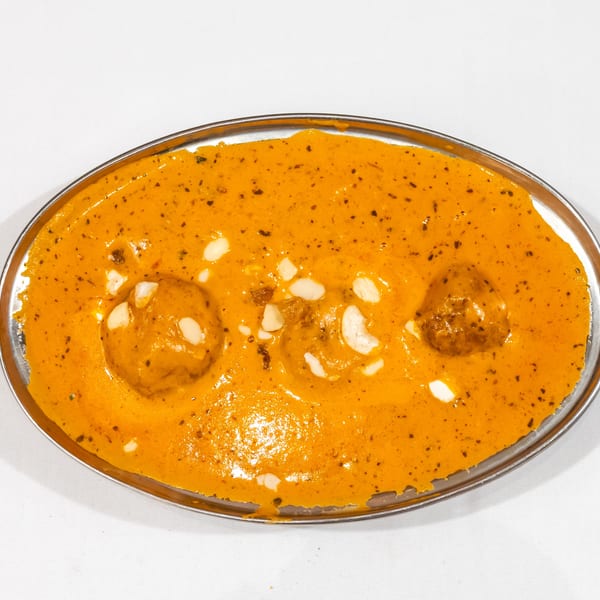Creamy orange curry with meatballs, cashews, raisins, and herbs served in an oval metal dish.