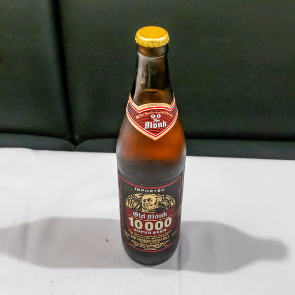 Bottle of Old Monk 10000 Super Beer standing on a white table against a dark upholstered background.