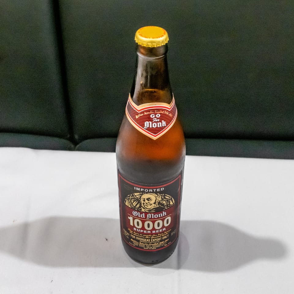 Bottle of Old Monk 10000 Super Beer standing on a white table against a dark upholstered background.